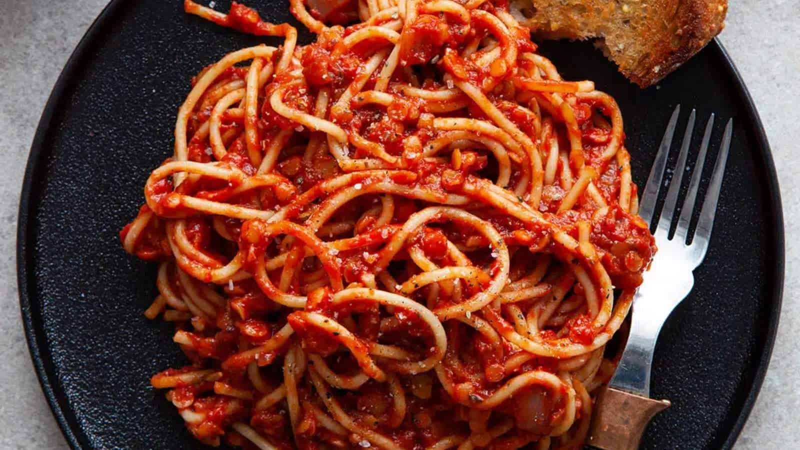 Spaghetti with tomato sauce and bread on a black plate.
