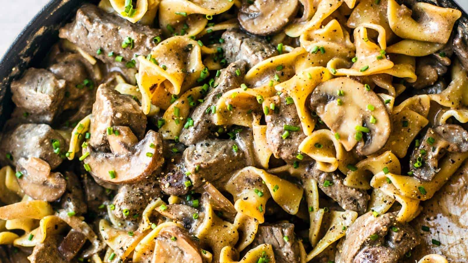 Beef stroganoff in a skillet with noodles and parsley.
