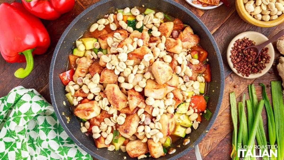 A skillet with chicken, peppers and other ingredients on a wooden table.