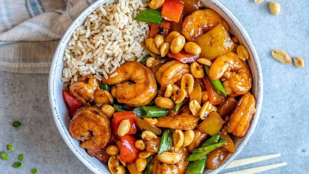 A bowl of stir fried shrimp with peanuts and vegetables.