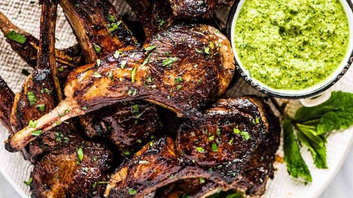 Grilled lamb chops with pesto sauce on a white plate.