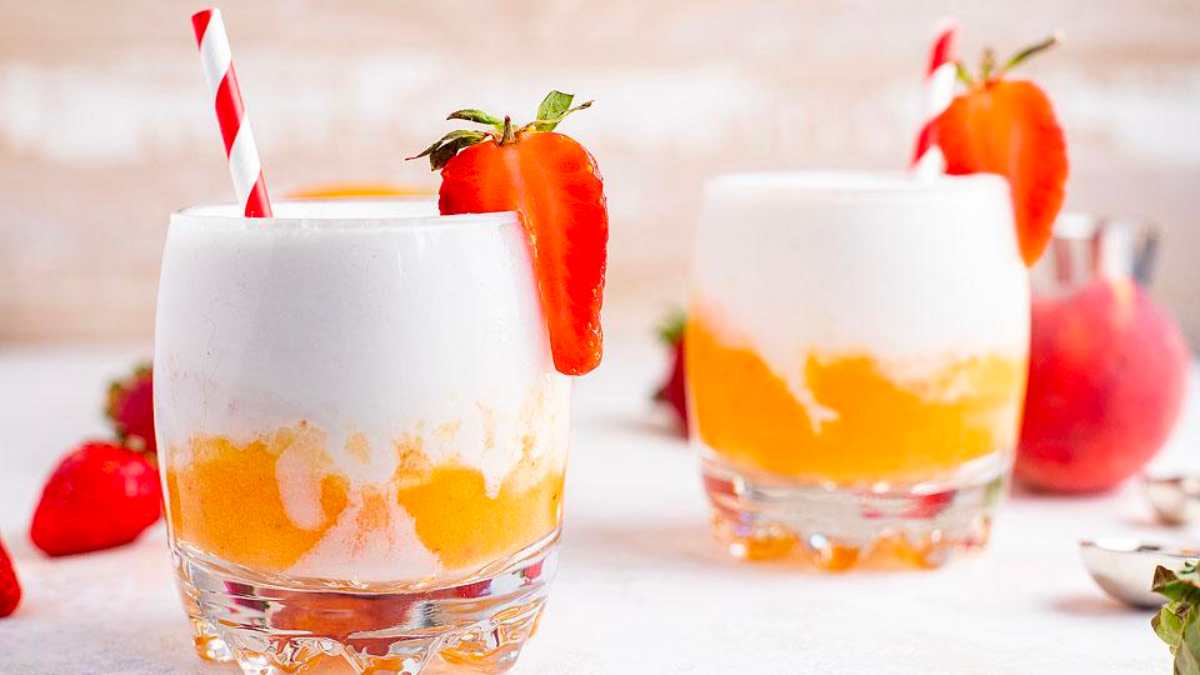 Two glasses of peach milkshake with strawberries and whipped cream.