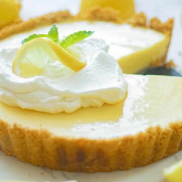 A lemon tart with whipped cream and lemons on a white plate.