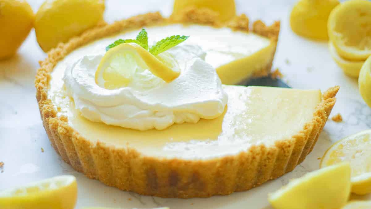 A lemon tart with whipped cream and lemons on a white plate.
