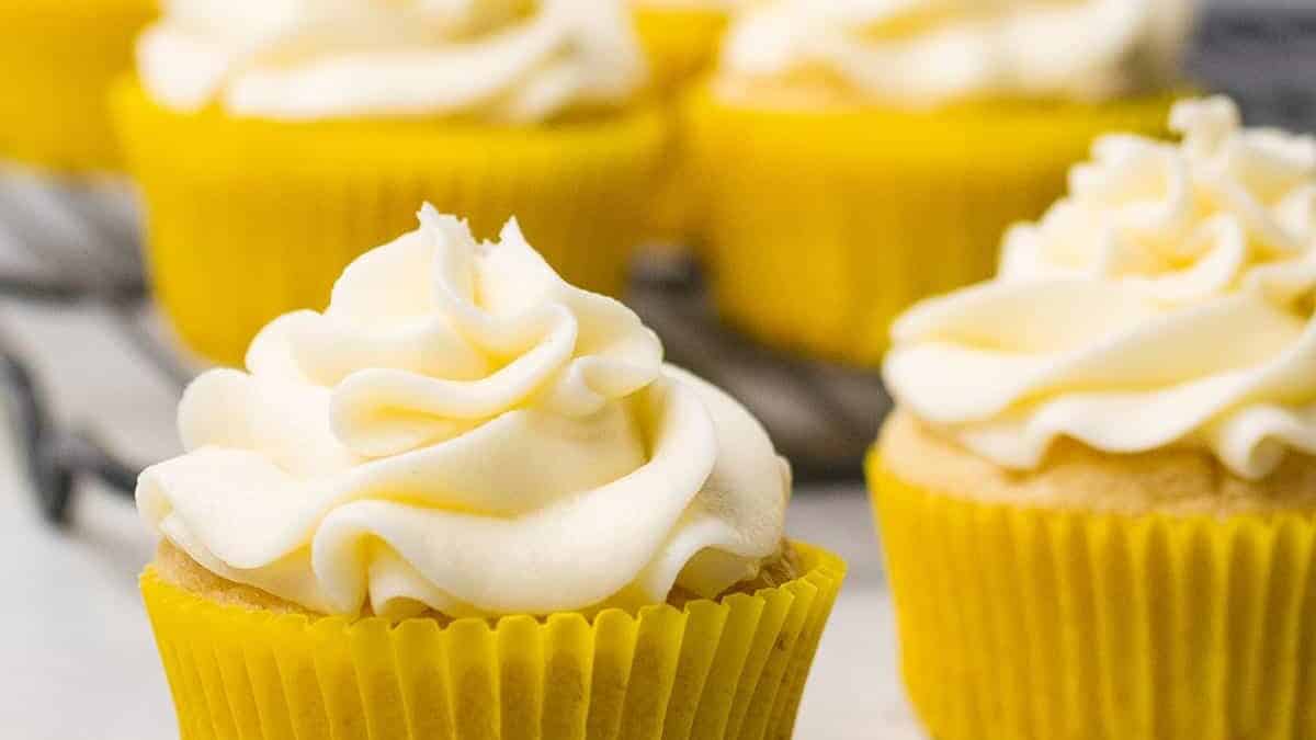 Yellow cupcakes with white frosting on a cooling rack.