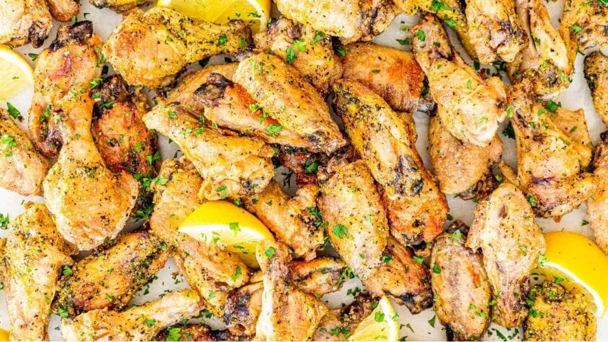 Chicken wings on a baking sheet with lemon wedges.