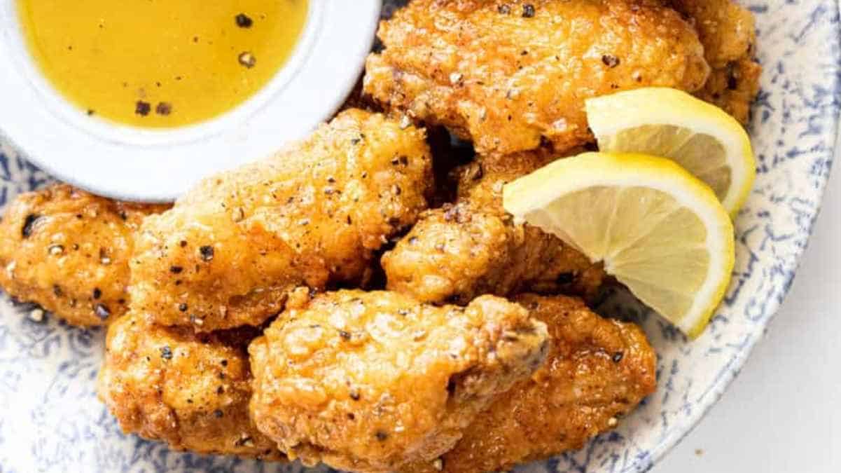Fried chicken wings on a blue plate with lemon wedges.