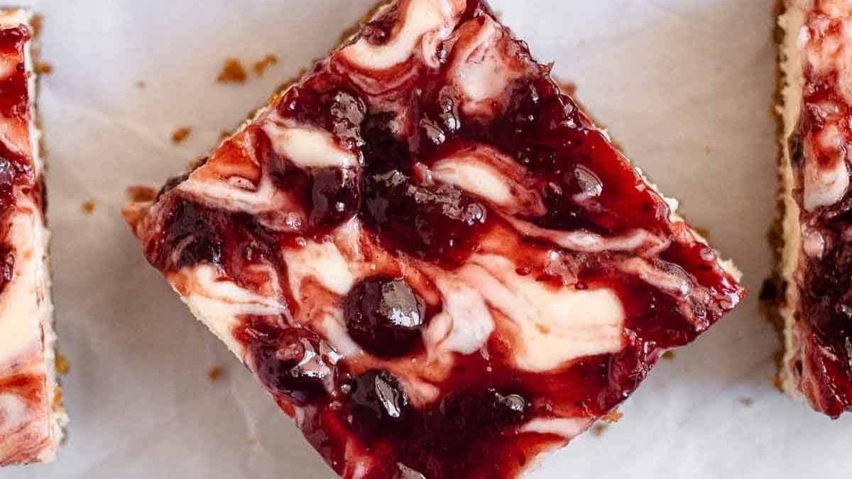 Three squares of cherry cheesecake bars on a piece of paper.
