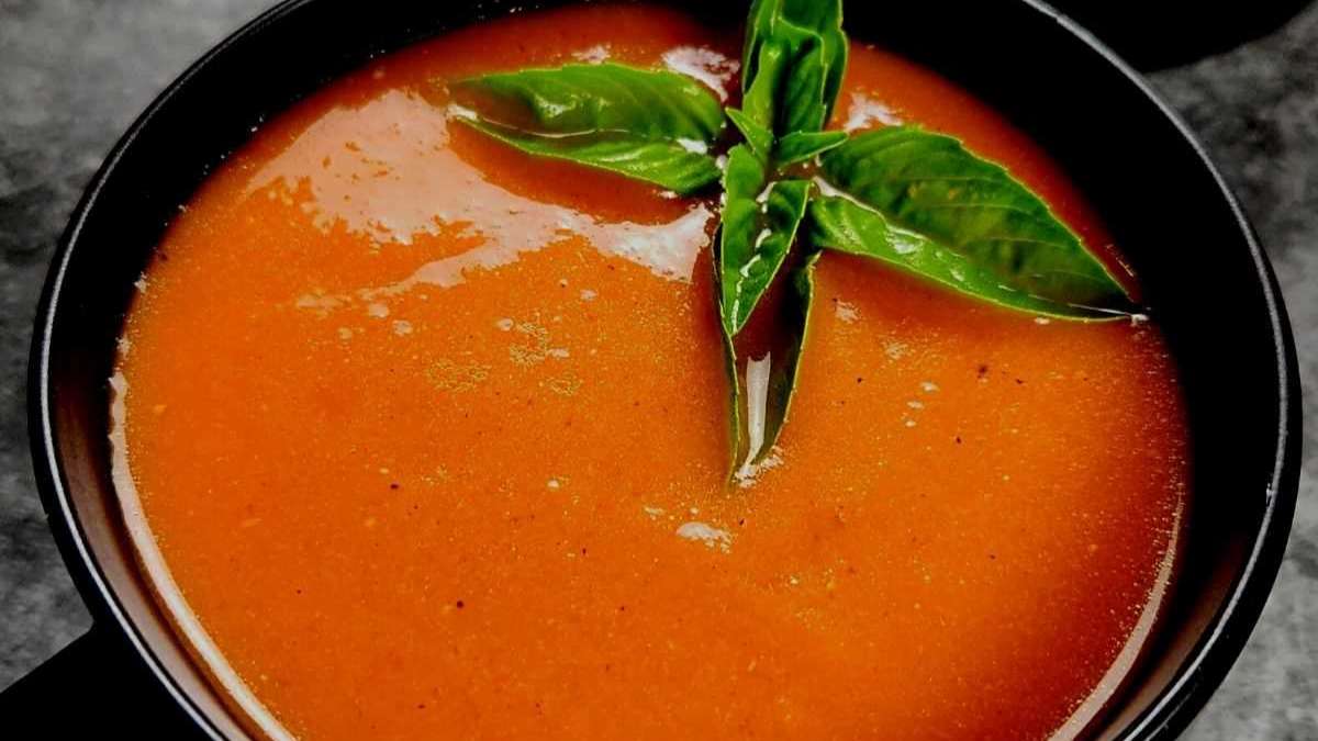 A bowl of tomato soup with basil leaves.