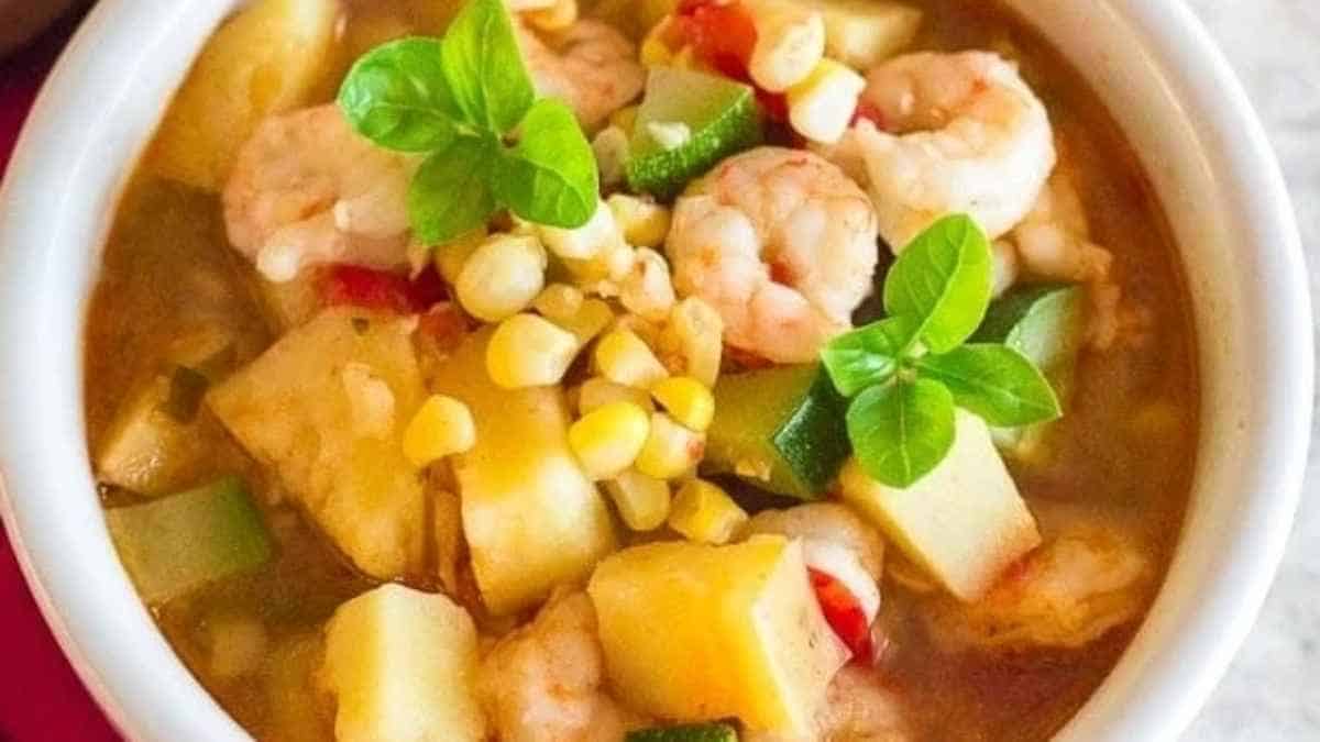 A bowl of soup with shrimp, corn and potatoes.