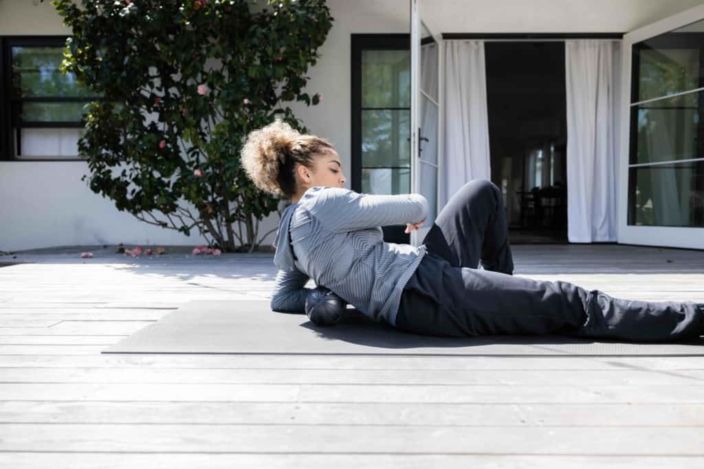 A woman laying on a yoga mat on a deck.