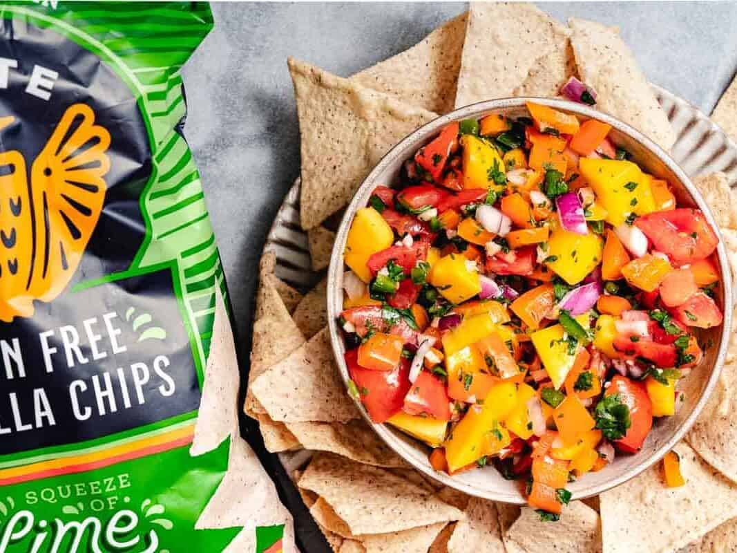 A bowl of salsa with a bag of chips next to it.
