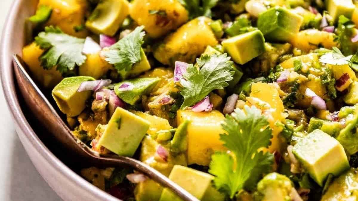 A bowl of mango and avocado salad with a spoon.