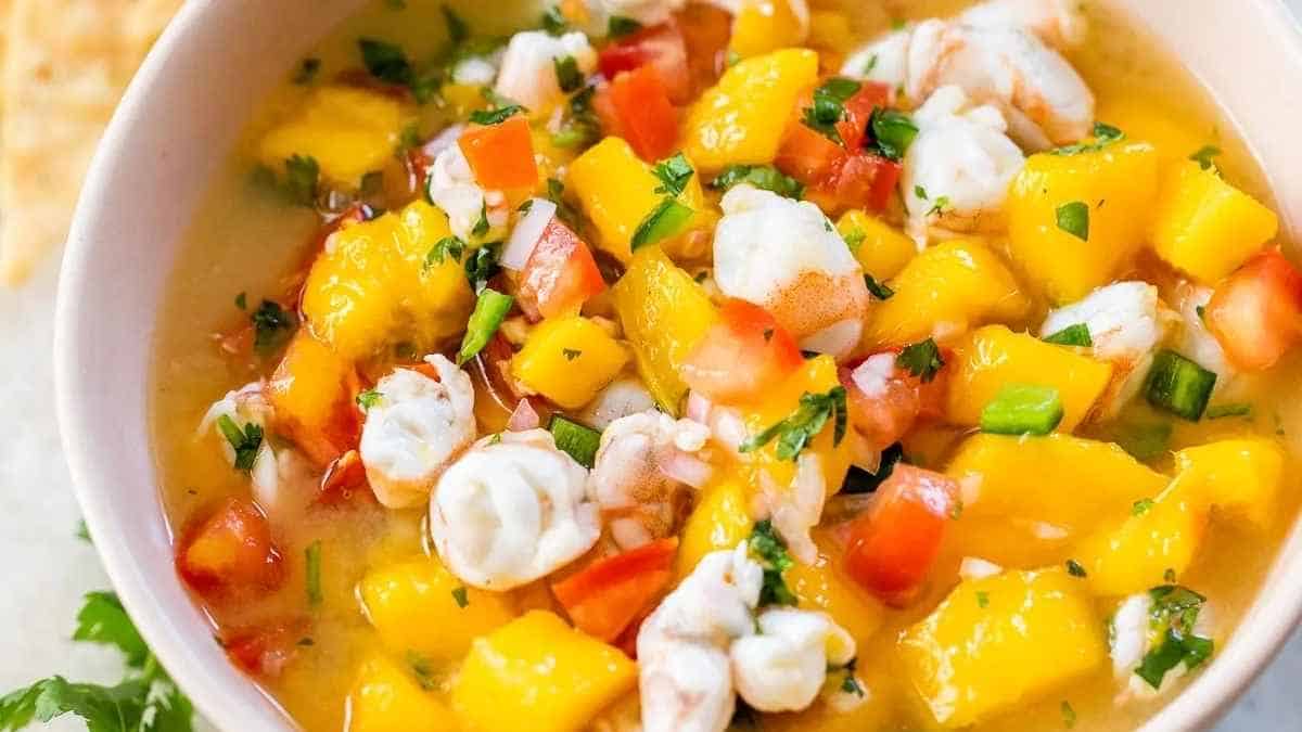 A bowl of mango salsa with shrimp and tortilla chips.