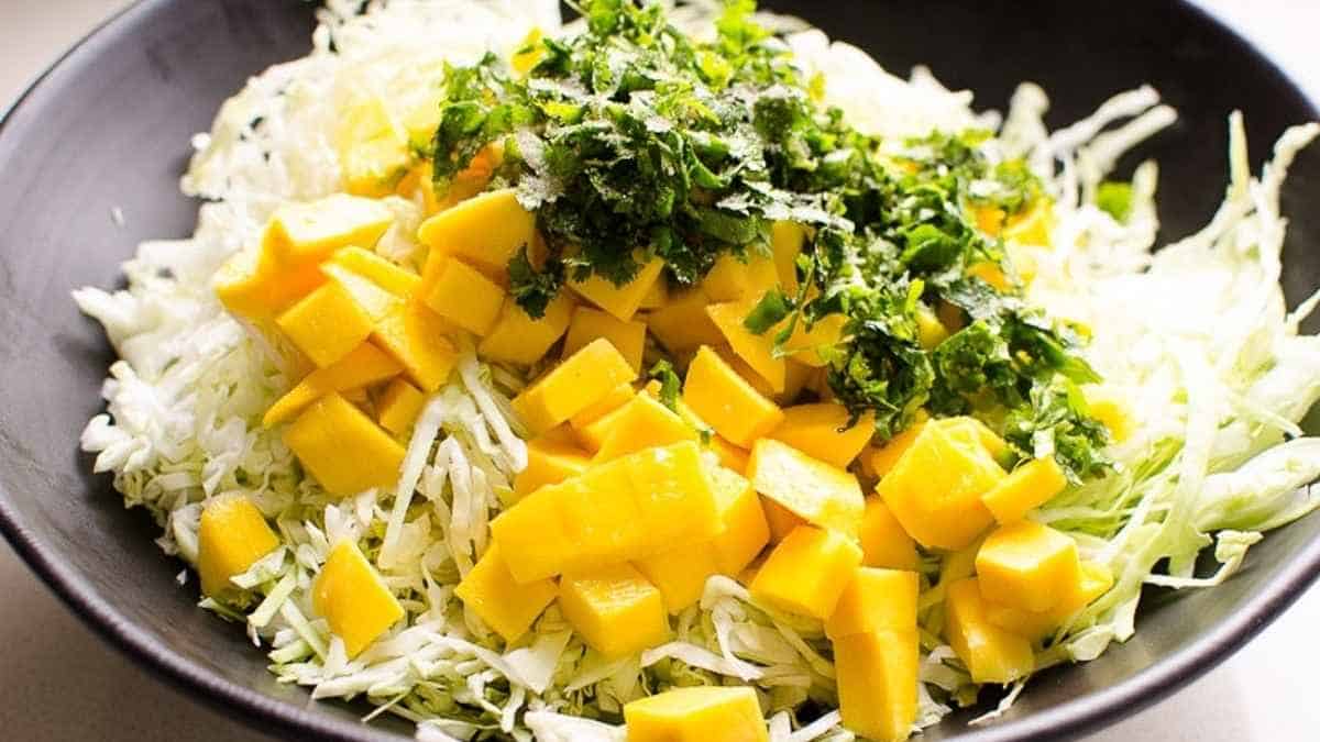 A bowl of mango salad with shredded cabbage and parsley.