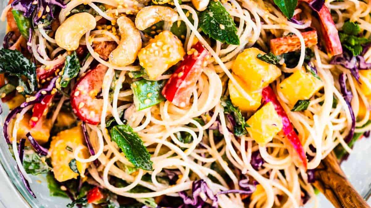 A bowl of noodles with vegetables and cashews.