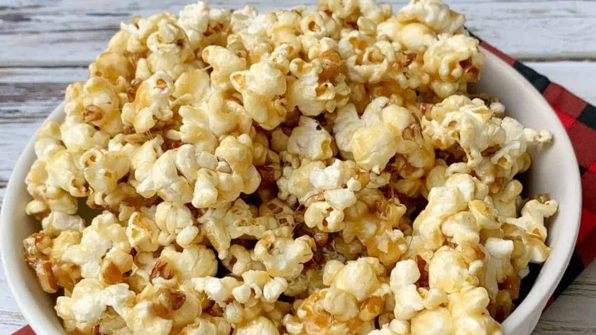 Caramel popcorn in a white bowl on a red checkered napkin.