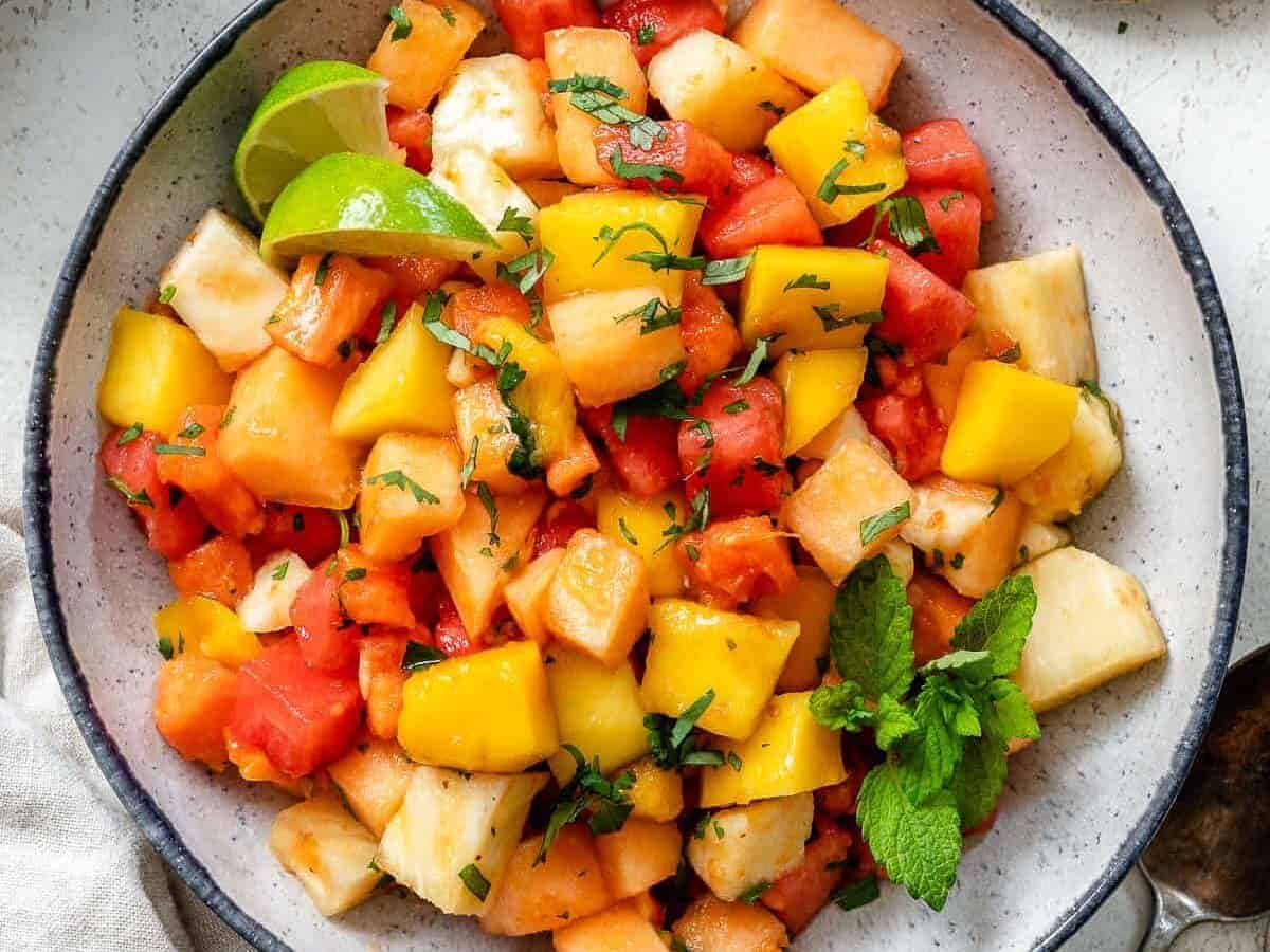 A bowl of fruit salad with lime and cilantro.