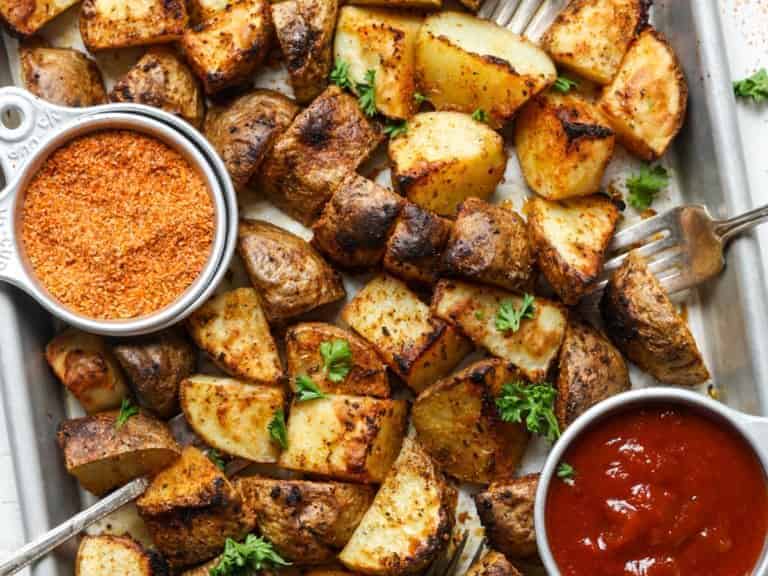 Roasted potatoes on a baking sheet with sauce and forks.