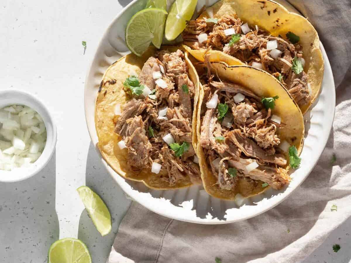 Pulled pork tacos on a plate with lime wedges.