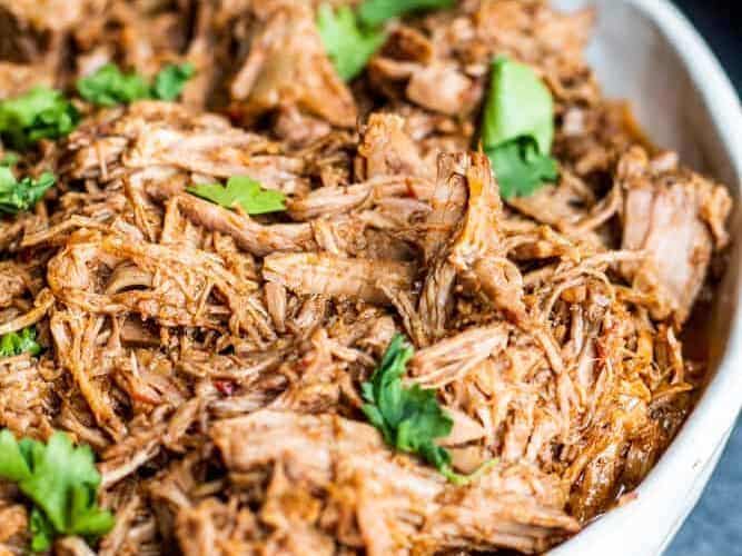 Slow cooker pulled pork in a white bowl with lime wedges.
