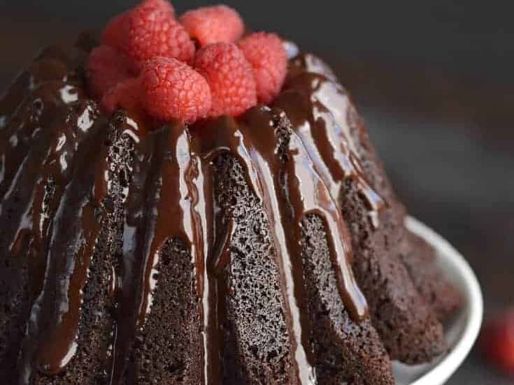 A chocolate bundt cake with raspberries on a white plate.