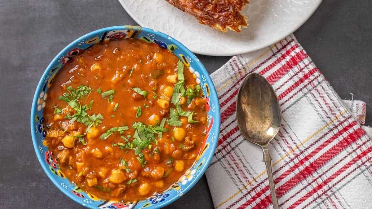 A bowl of chickpea stew and bread on a table.