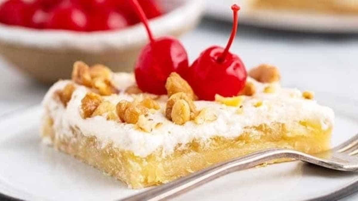 A slice of pineapple cake with whipped cream and cherries on a plate.