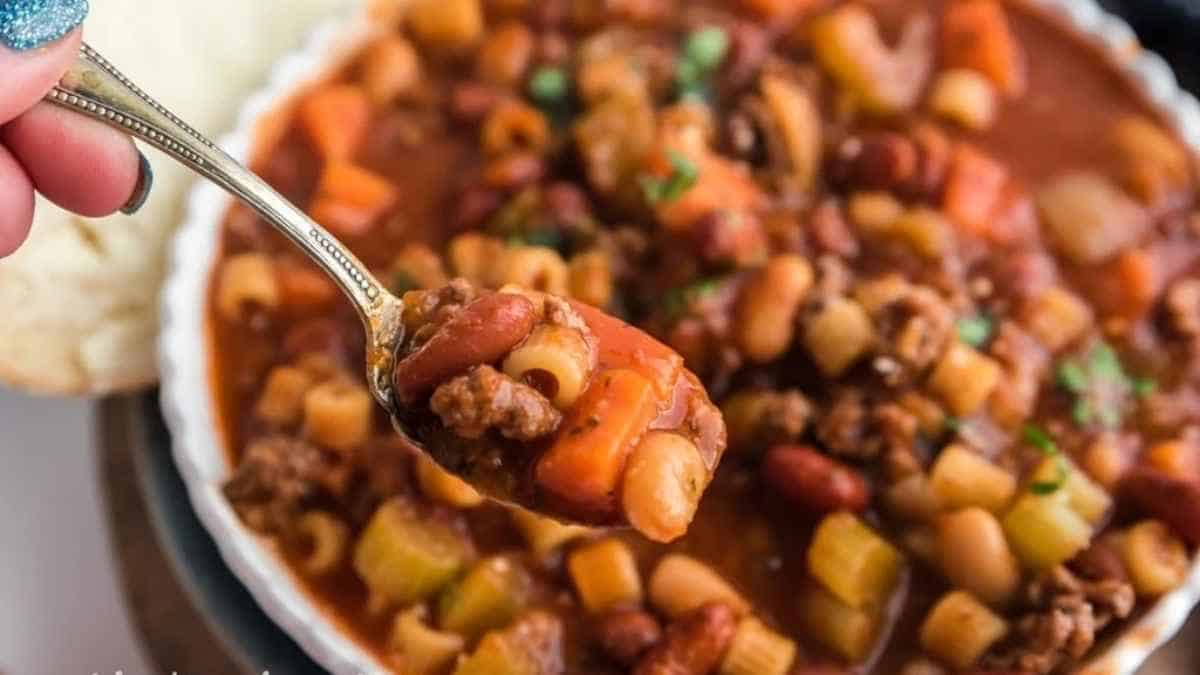 A person is holding a spoonful of chili and pasta.