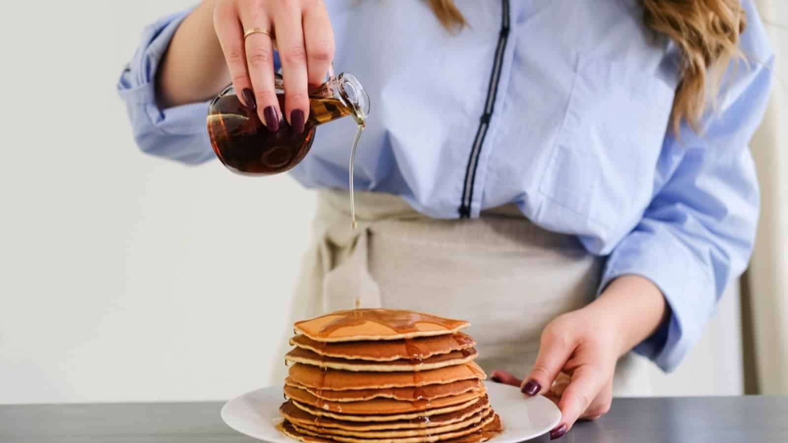 A woman pouring syrup on a stack of pancakes.