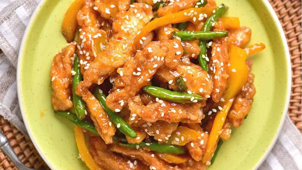 A plate of stir fried chicken with green beans and sesame seeds.