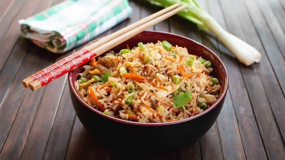 A bowl of fried rice with vegetables and chopsticks.