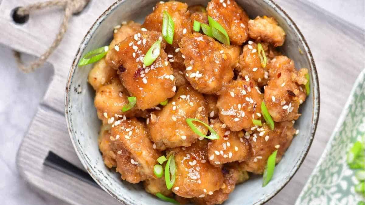 A bowl of asian chicken with sesame seeds and green onions.