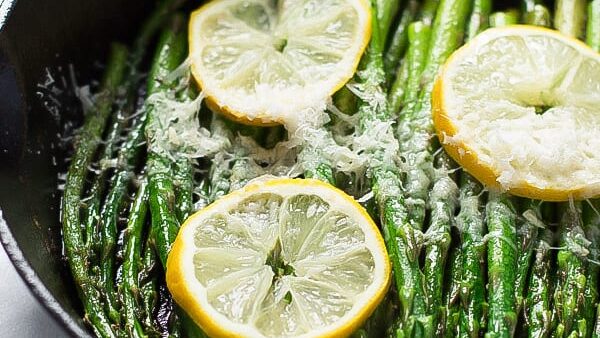 Asparagus in a skillet with lemon wedges and parmesan cheese.