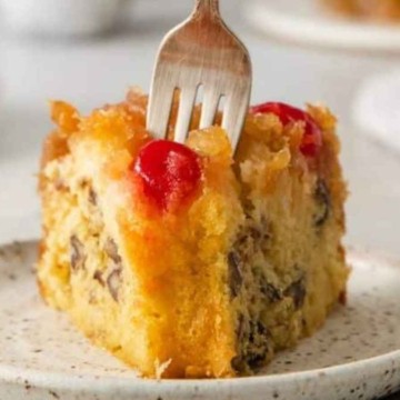 A slice of pineapple upside down cake on a plate with a fork.