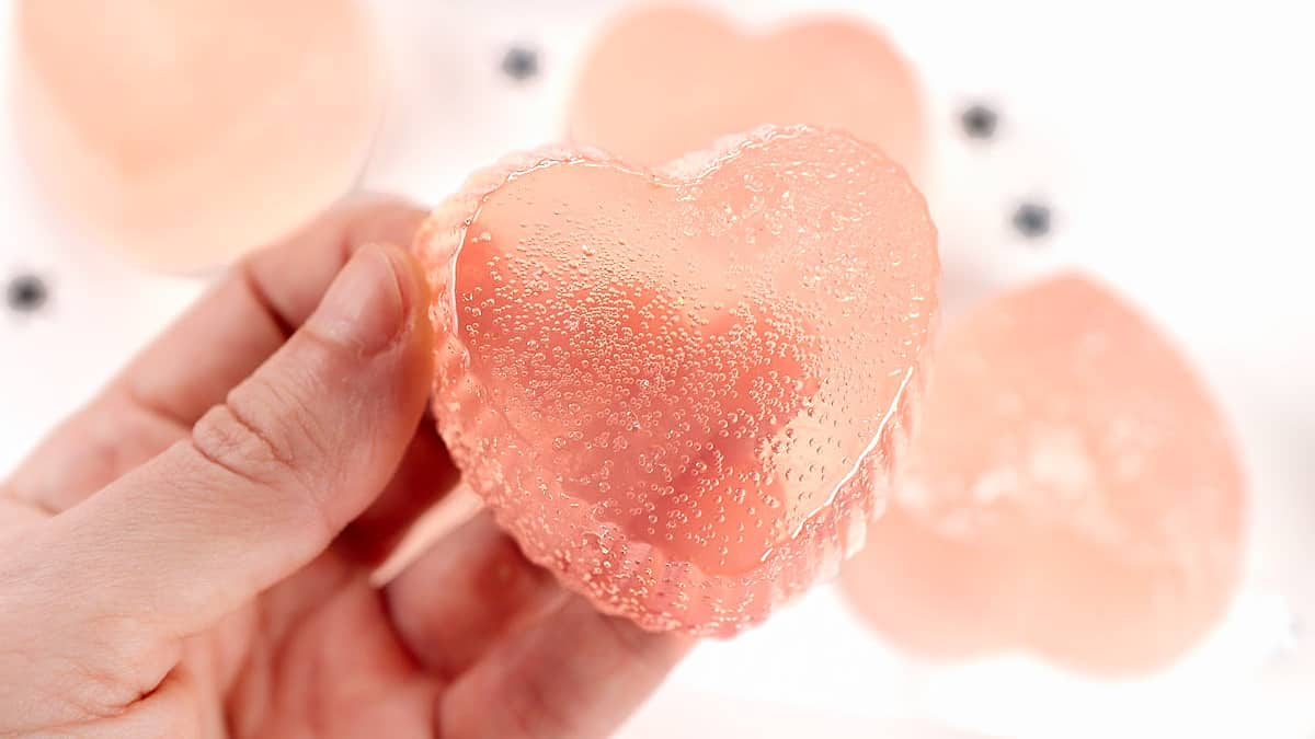 A person holding a pink heart shaped ice cube on a plate.