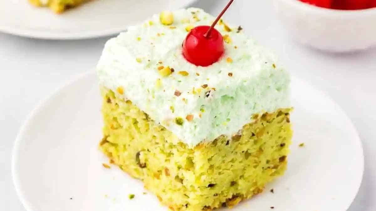 A slice of pistachio cake on a plate with a cherry on top.