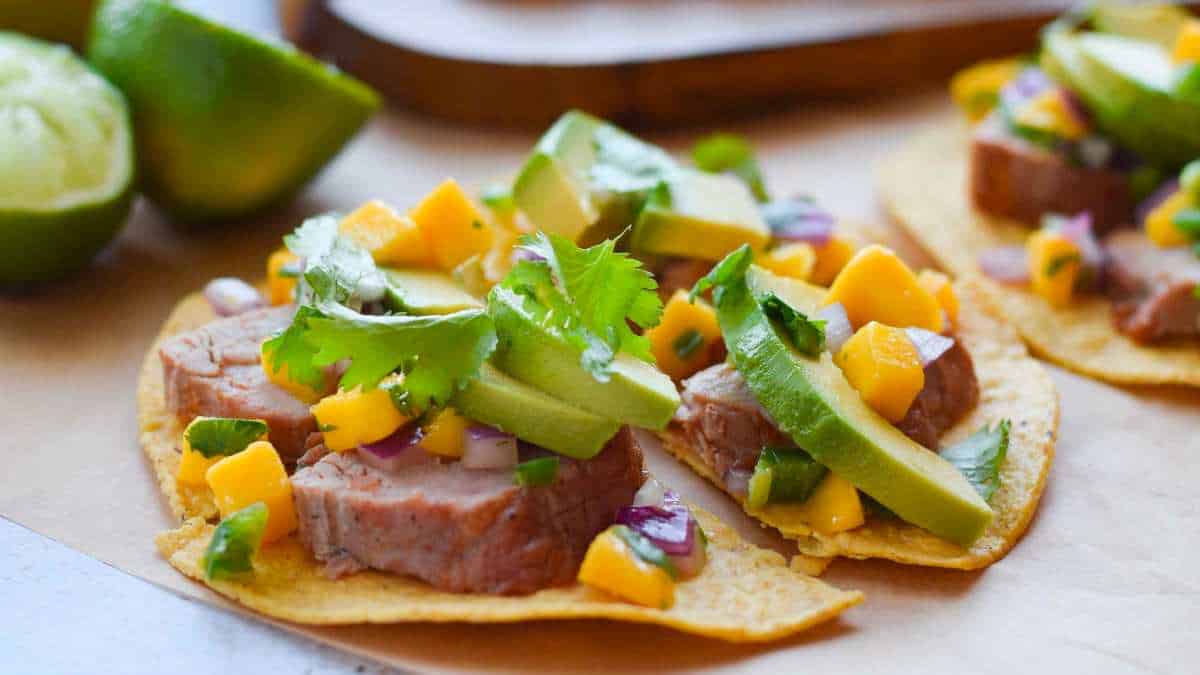 Two tacos with meat and mango on a wooden board.