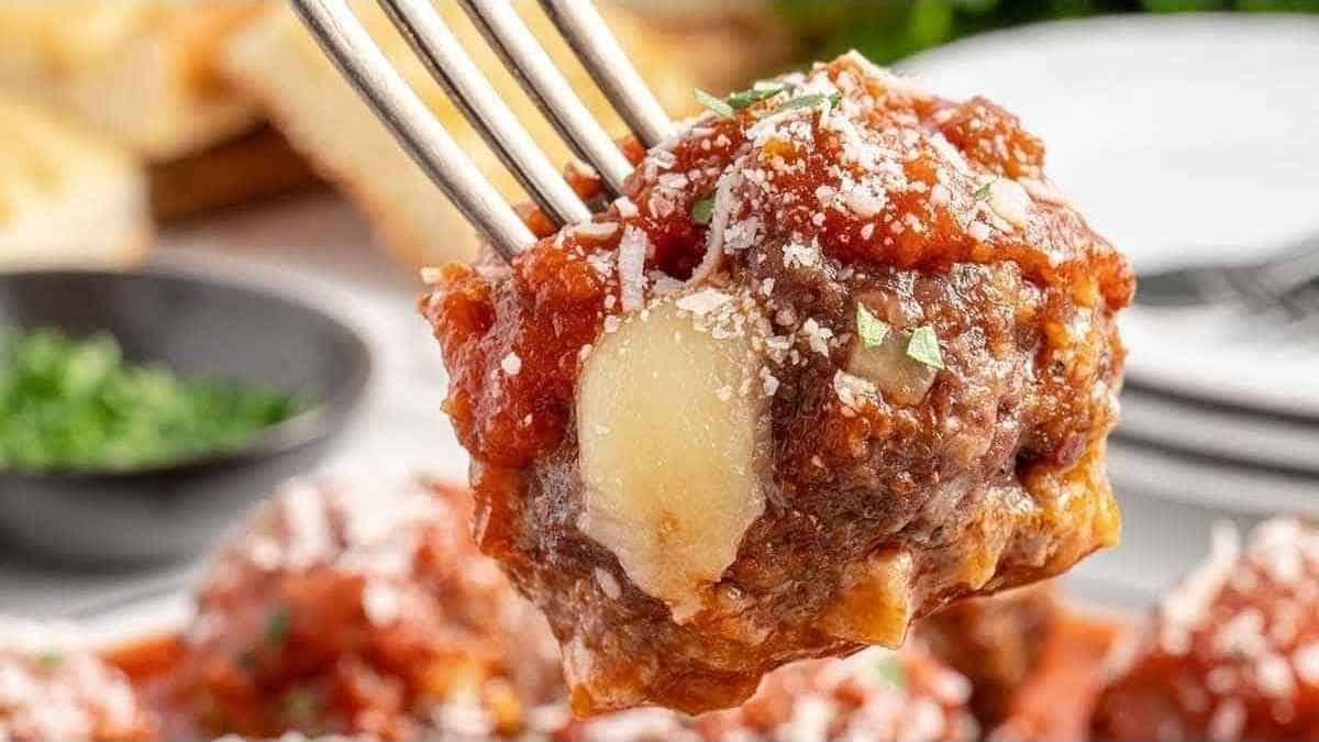 Meatballs on a fork with cheese and sauce.