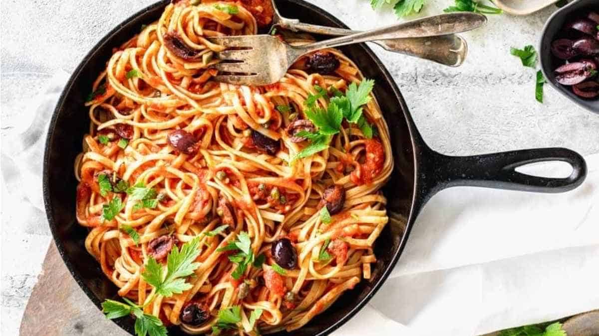 A skillet full of spaghetti with tomatoes and olives.