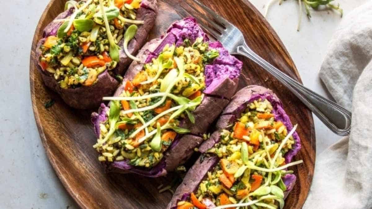 Three purple sweet potatoes on a wooden plate.