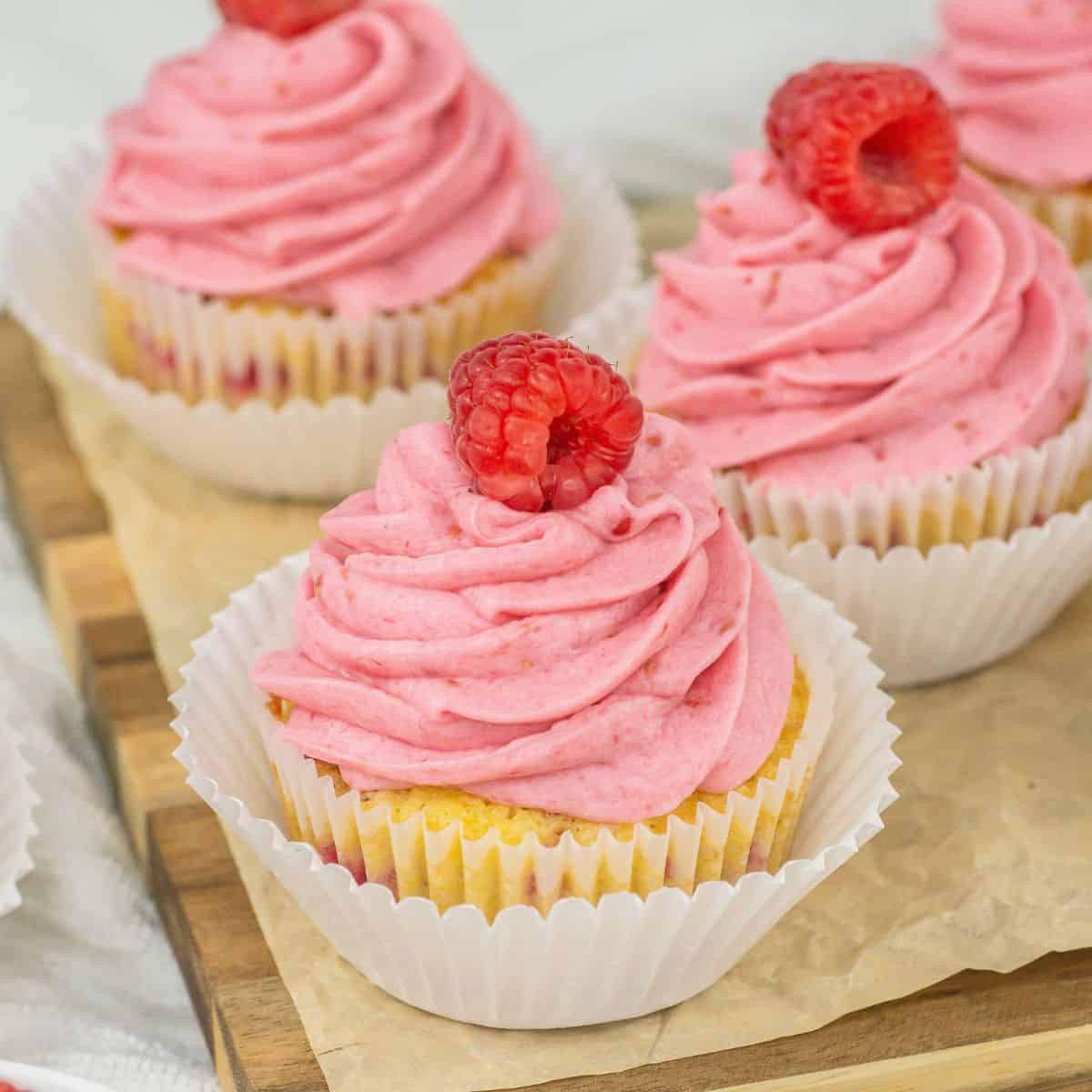 Pink cupcakes with raspberry frosting on a wooden cutting board.