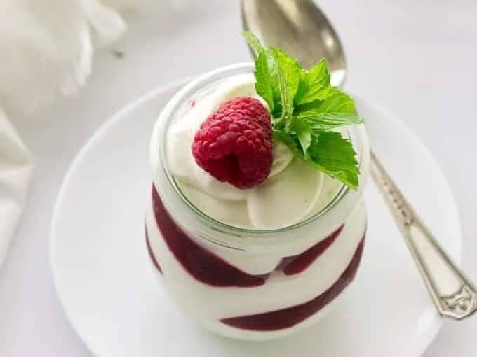 A cup of raspberries and whipped cream on a white plate.