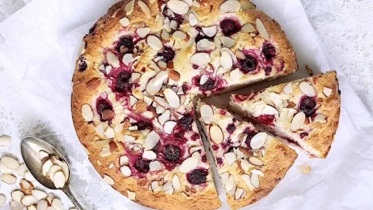 A cranberry and almond cake with a slice taken out.