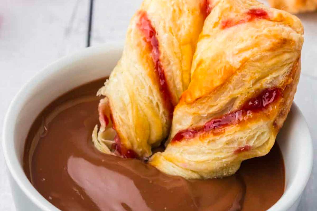 A chocolate croissant with raspberry sauce in a white bowl.