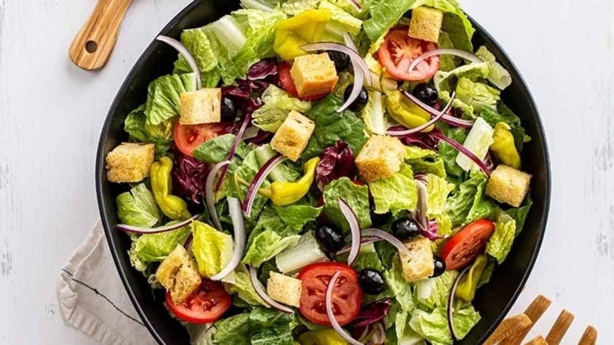 A salad with olives, tomatoes and croutons in a pan.