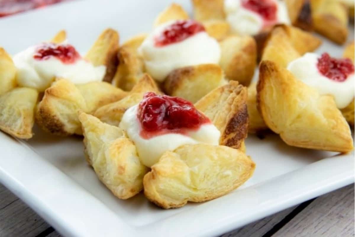 A plate topped with mini pastries with jam and cream.