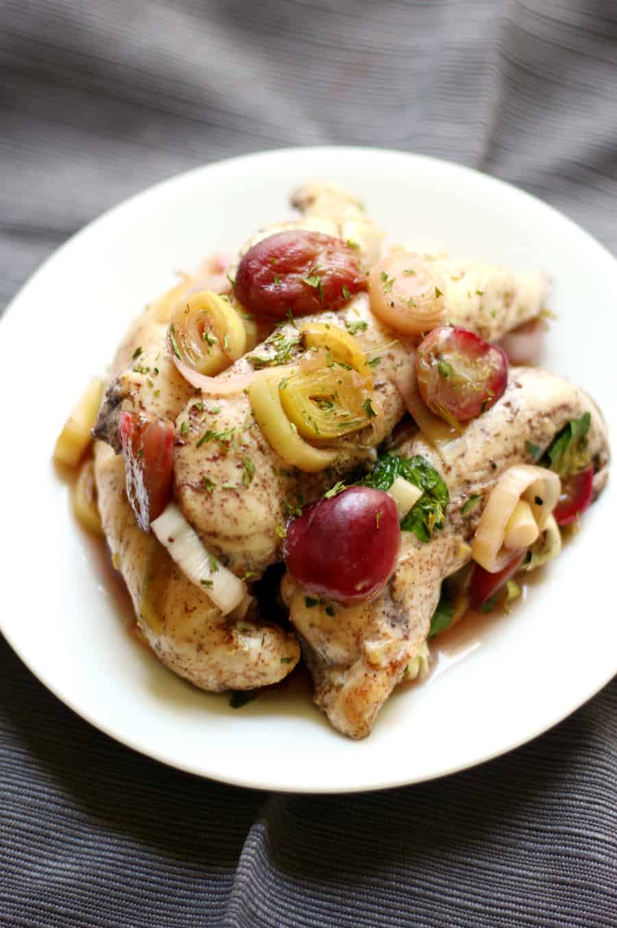 A plate with tender chicken and grapes on it.
