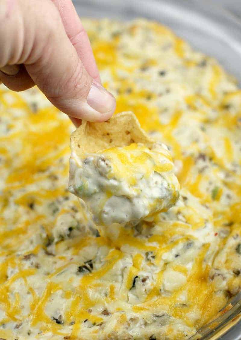 A person dipping a chip into a bowl of ground sausage cheese dip.