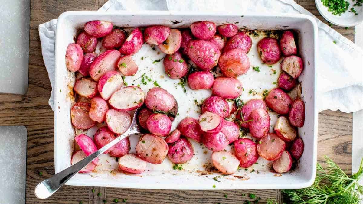 Roasted red potatoes in a baking dish with a spoon.